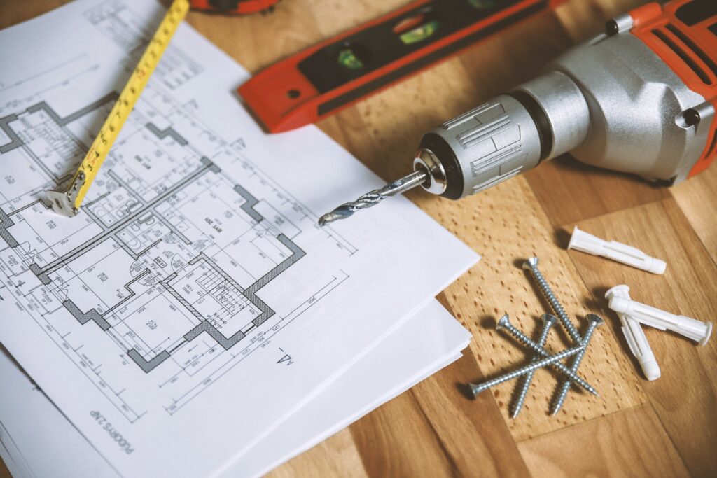 Floor plans on a wooden table with a tape measure, a drill, a spirit level, screws and wall plugs