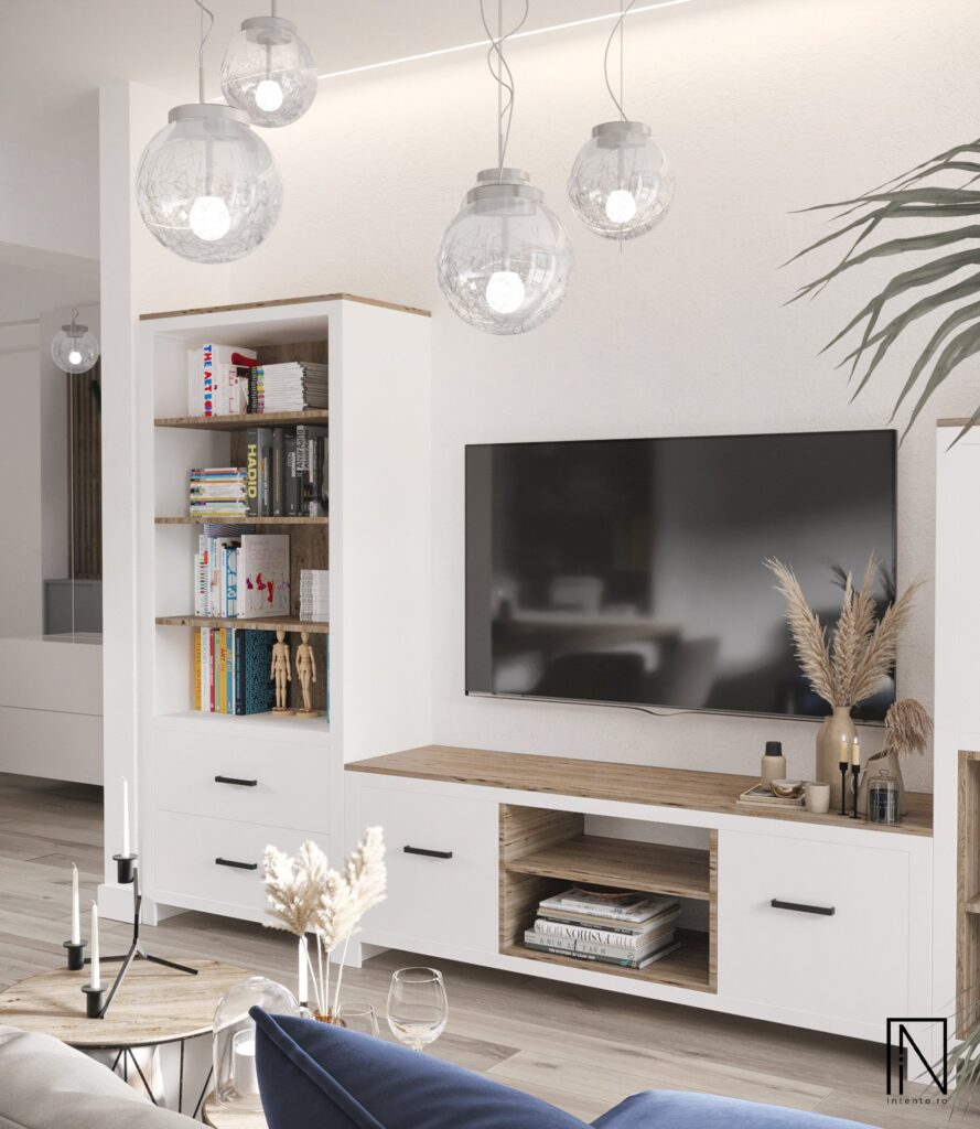 Mobilier TV alb cu rafturi din lemn și cărți, mânere negre, lustre glob din sticlă și decor cu iarbă de pampas