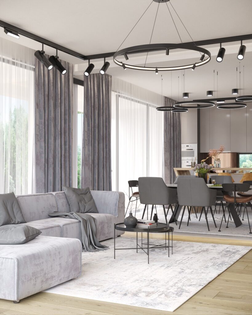 Randare a zonei de zi și de dining deschise, cu canapea gri modulară, lustre-inel și bucătăria în fundal