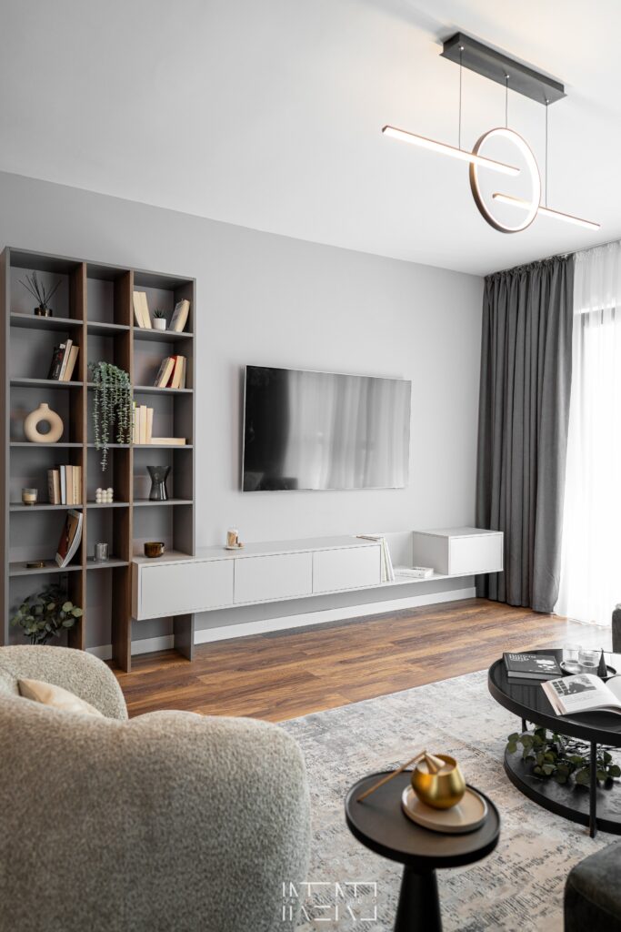 Peretele TV din living cu comodă albă suspendată, bibliotecă înaltă deschisă și o lustră LED în formă de inel