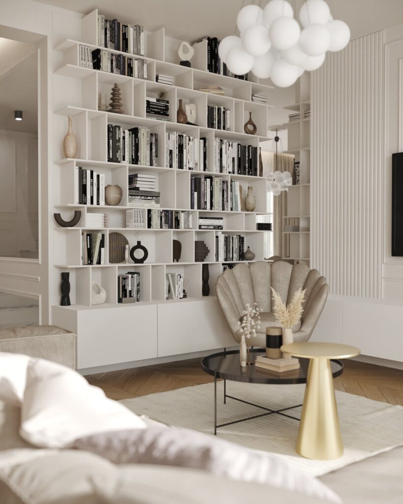 Bibliotecă albă deschisă cu cărți și obiecte ceramice, fotoliu scoică, măsuță neagră și măsuță aurie sub candelabrul cu globuri